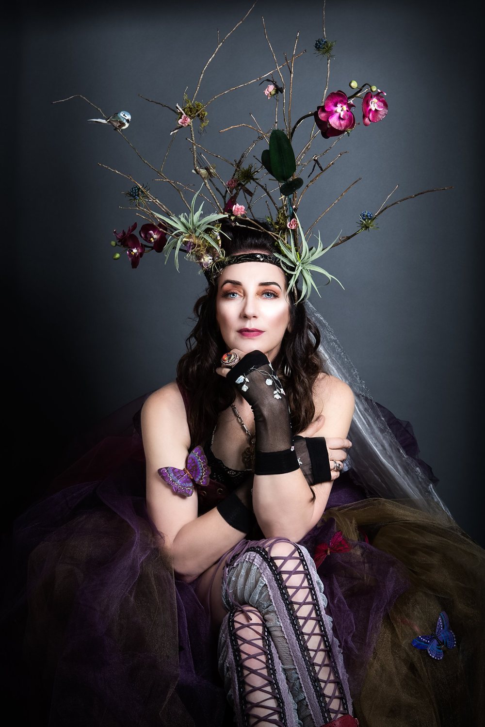 Portrait of Nymphya in a crown of twigs, orchids and air plants with butterflies on her arm and skirt