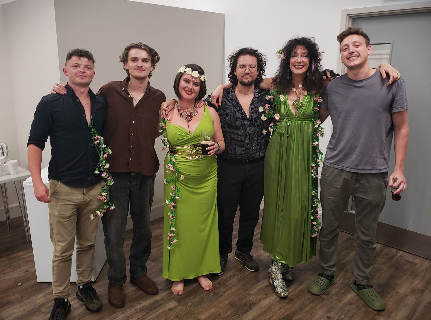 The Dreamery company backstage: Nymphya and the band, arms around each other, smiling in green and woodland flowers