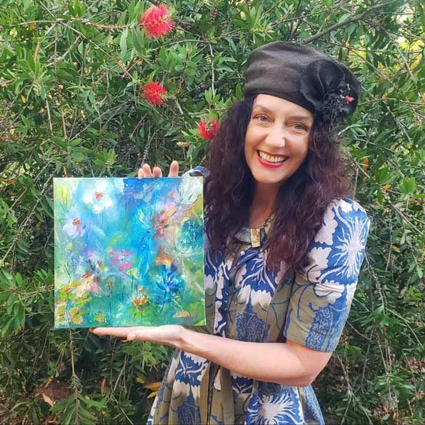 Nymphya smiling beside flowering shrubs, holding the Kaleidoscope of Spring Blooms painting